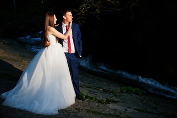 Fototapeta premium Lovely wedding couple against waterfall on sunset at Carpathian mountains.