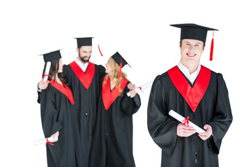 Young student in graduation cap with diploma and friends standing behind isolated on white