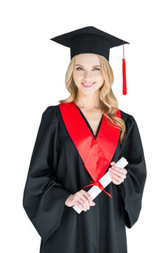 Beautiful young woman in academic cap holding diploma and smiling at camera