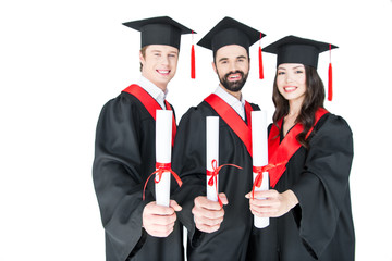 Happy students in graduation caps holding diplomas and smiling at camera