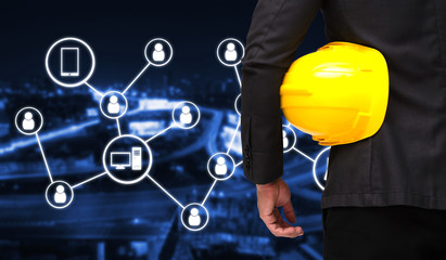 back view of smart businessman in black suit with yellow safety helmet with icon social media concept on blurred night city background,