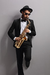 Fototapeta na wymiar Jazzer playing on a saxophone and leaning against gray wall
