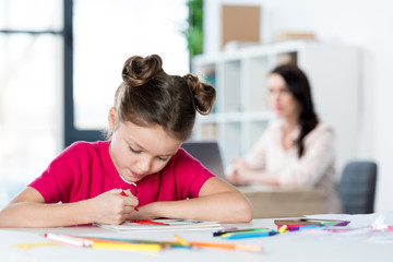 Concentrated little girl sitting at table and drawing with pen