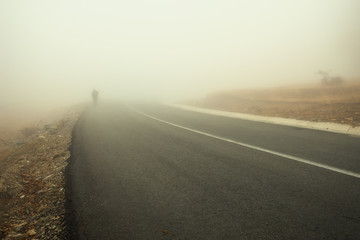 Distant silhouette of a man approaching on the side of the highway through the thick fog