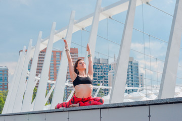 Woman doing yoga exercises outdoors in the city.Beautiful brunette fit young woman wearing sportswear practicing yoga urban style.Asana, working out,fitness,sport,training and lifestyle concept