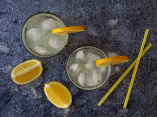 Obraz na płótnie Canvas glasses of cold homemade lemonade with lemon slices, ice cubes and straws on dark background. Copy space