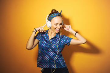 close-up portrait of a girl on a yellow background in studio beautiful young bright sexy hair in a ponytail, wearing headphones listening to music and singing and posing with red lips and manicure