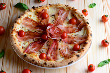 Top view of neapolitan pizza with bacon, mozzarella and cherry tomatoes, served on a wooden table for a dinner in italian restaurant. Italy food. Pizza from wooden oven. Close up. 