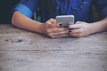 A woman holding and using smart phone on wooden table with feeling relax while sitting in vintage cafe 