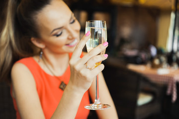 close-up portrait of a beautiful young elegant sexy blonde woman in the cafe with a glass of champagne,White wine smiling and drink posing, with a ring on her finger, she is engaged