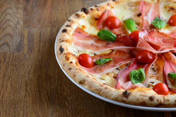 Neapolitan pizza with bacon, mozzarella, cherry tomatoes and cream sauce, served on a wooden table for a dinner in italian restaurant. Italy food. Pizza from wooden oven. Close up. Macro.