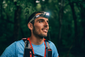 Fit male jogger with a headlamp rests during training for cross country trail race in nature park.