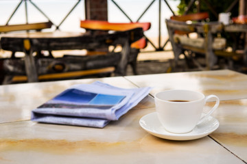 Close up white coffee cup on table at sunrise sand beach with newspaper in the morning