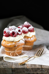 Muffins with soft cream and fresh raspberry powdered with sugar, rustic background