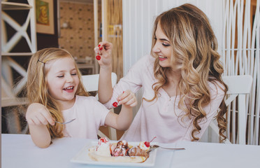 Little girl with mom and feed each other cherries ice cream in a cozy cafe.Good relationship of parents and child. Happy moments together.