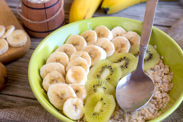 Breakfast oatmeal with banana and kiwi on a wooden background in a green plate.
