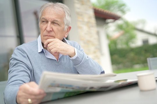 Senior Man Reading Newspaper Outside In Yard