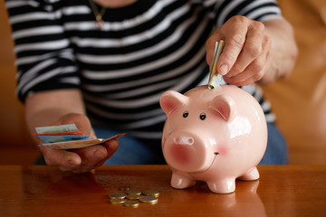 Senior woman putting money into small piggy bank