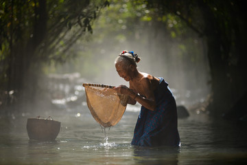 Old woman fisherman casting fish in river ,Thailand