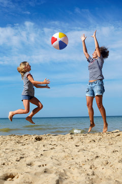 Happy parent and child play a ball at coast on a sunny summer day. Beach sports