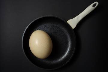 Ostrich egg on a frying pan at black background 