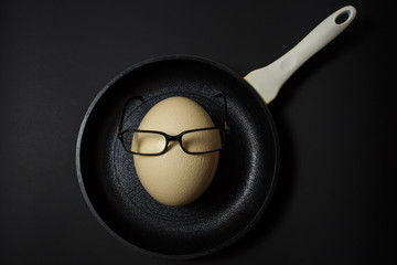 Ostrich egg with glasses in pan on black background