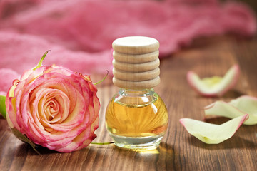 Fototapeta na wymiar Rose essential oil in glass bottle on wooden background