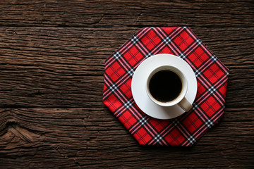 cup of coffee and red checkered kitchen tablecloths on wooden surface in top view