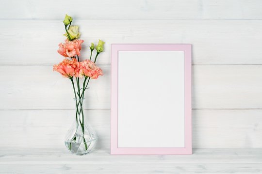 Flowers in vase and a photo frame on a wooden background.