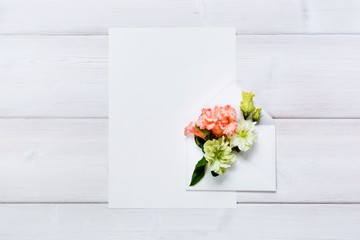 Colorful spring flowers in envelope and white sheet on wooden background.