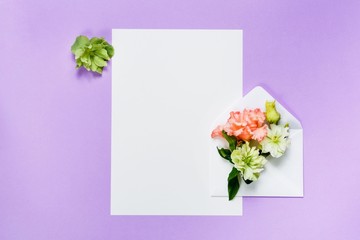 Colorful spring flowers in envelope and white sheet on violet background.