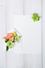 Colorful spring flowers in envelope and white sheet on wooden background.