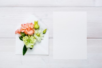 Colorful spring flowers in envelope and white sheet on wooden background.