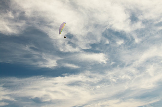 A paraglider flies on background blue sky.