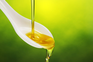 extra virgin olive oil poured in a spoon overflowing on green background