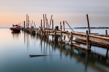 Fototapeta premium Old wood bridge for small fishing boat in the sea with sunset 