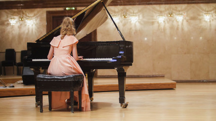 Cute teenager girl plays piano in the concert hall at scene