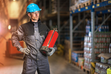 Caucasian warehouse worker with fire extinguisher. Safety concept.