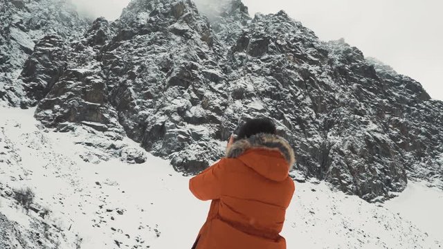 Beautiful girl makes a photo or selphy on smartphone. In the mountains in winter, adventure and travel. Handheld shot