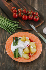 Potatoes and asparagus with tomatoes and tartar sauce on plate ready to eat.