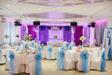 Served tables with a white tablecloth and chairs with white covers, decorated with blue bows