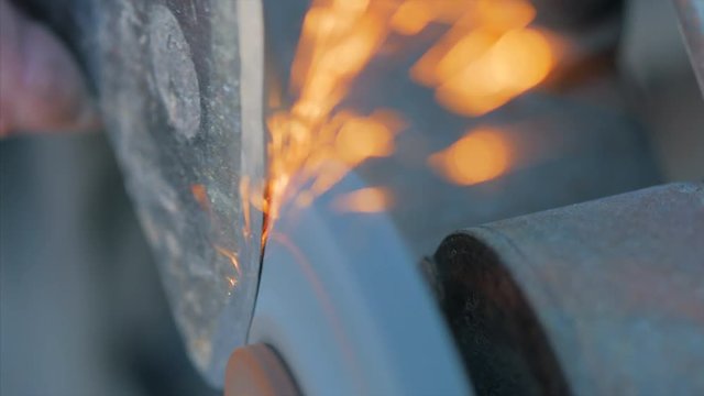 A man sharpens an ax on a machine with sparks.