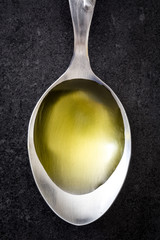 Olive oil on a spoon. Black slate background.

