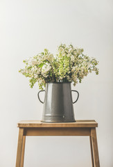 Spring bouquet of white lilacs in vintage gray enamel vase, white wall background behind, vertical composition