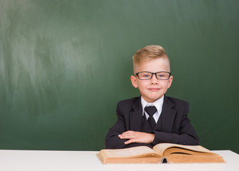 Portrait of a happy schoolboy with book near empty green chalkboard