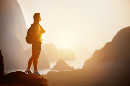 Beautiful woman with backpack at sunrise or sunset on mountain top