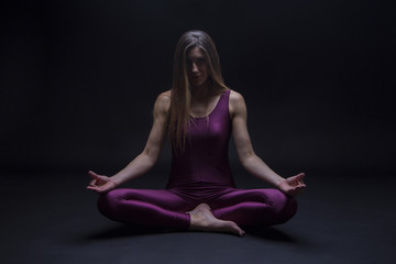 Young woman practicing yoga position in lotus flower, isolated on a dark background