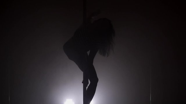 Silhouette of a young woman dancing with the pole slow motion