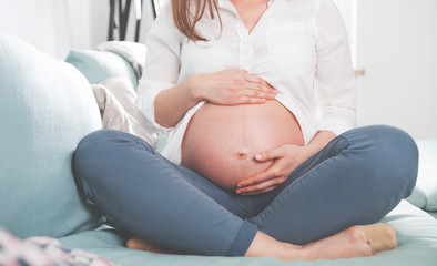 Pregnant woman sitting on sofa at home close up of belly
