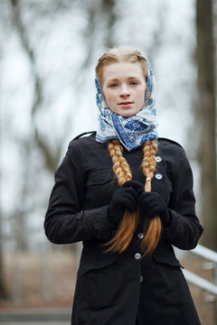 Emotional portrait of happy beautiful woman with red braids hair and natural makeup wearing black jeans trench grey sweater blue white headcraft enjoying her life in spring city park.